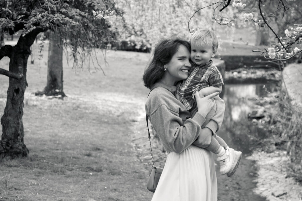 Black‑and‑white candid family photo with mother and son hugging during cherry blossom in New Jersey.