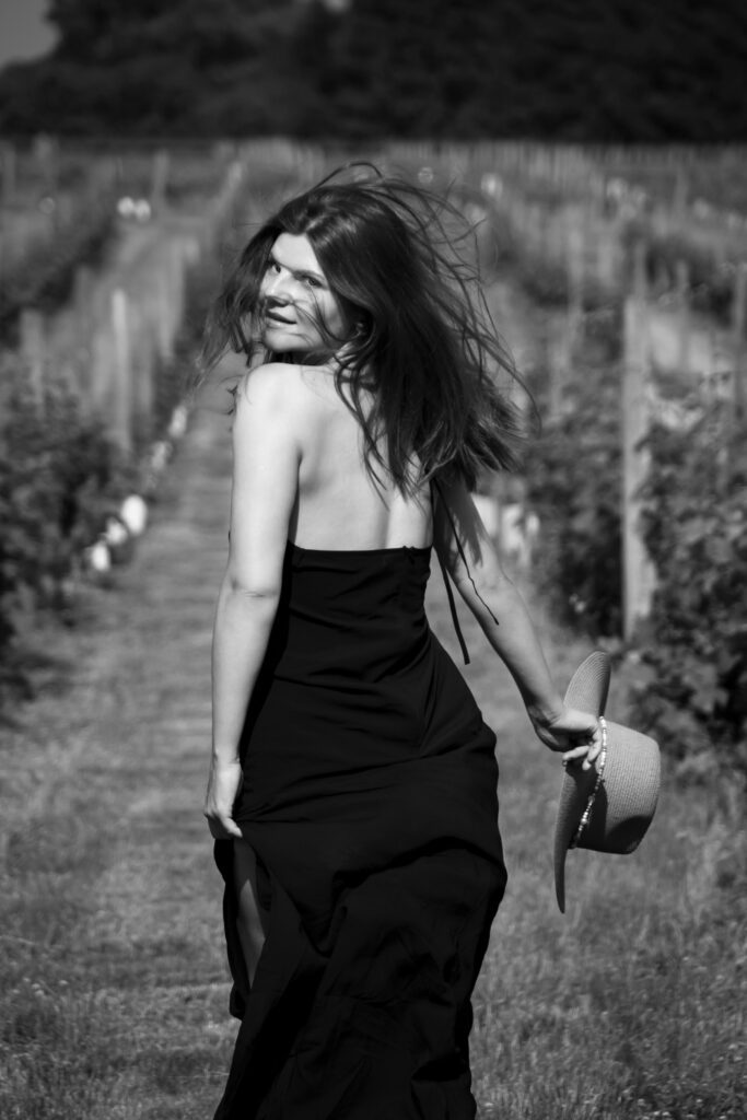 Girl’s Portrait 5 Portrait of a woman running away from the camera in a black dress, standing in a sunlit New Jersey vineyard.