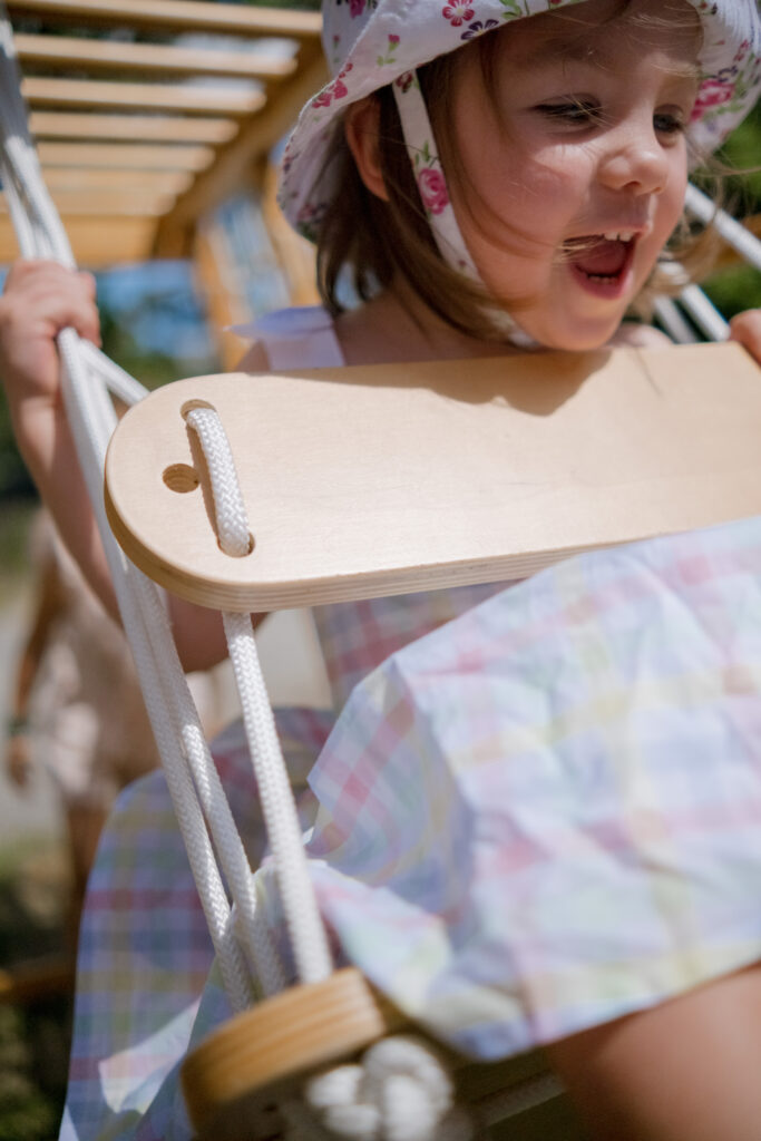 Kids 2 Close‑up portrait of a little girl in a hat, smiling on swings under bright summer light during birthday party