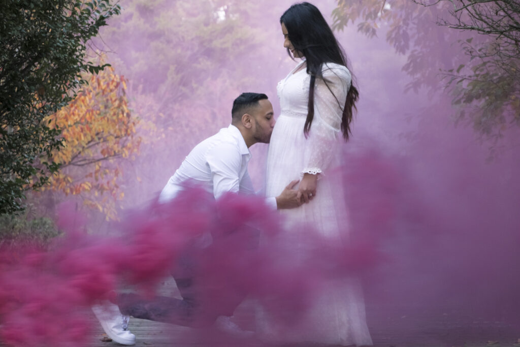 Mother to be 4 Photo of father kissing mother-to-be belly as pink smoke floats around them in NJ park.