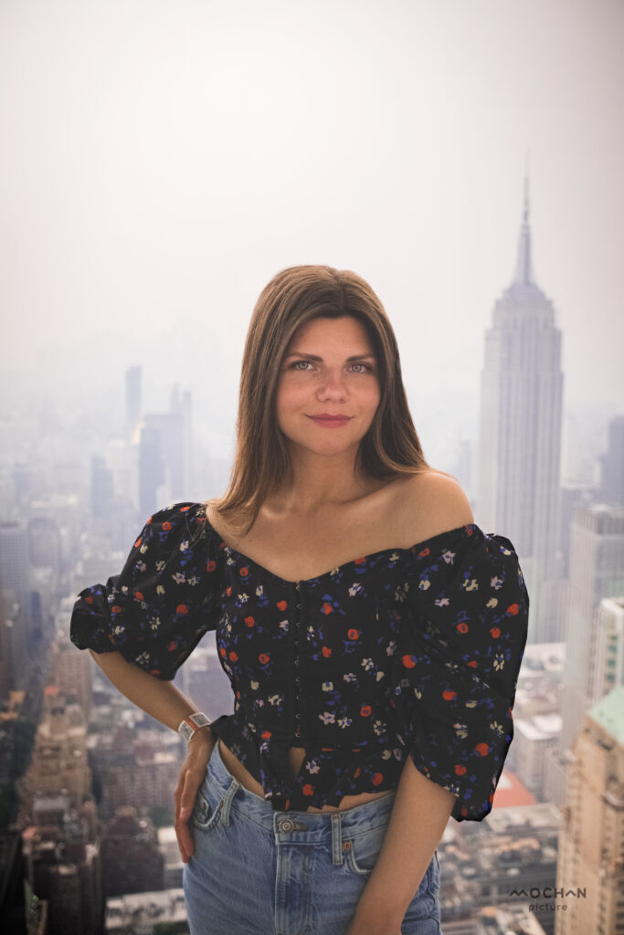 Portrait photo back Woman in floral blouse posing on a rooftop with New York City skyline in the background.